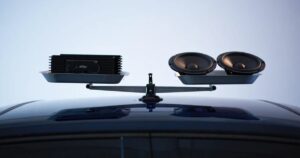 A balanced scale on top of a car with an amplifier on one side of the scale and two speakers on the other