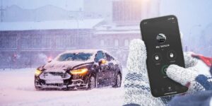 A person's hands pressing the start button for a remote start on their phone for their car which is covered in snow on a cold day