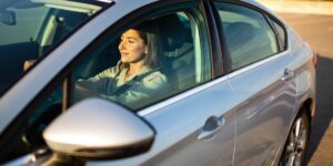A woman driving a gray car with the sun on her face